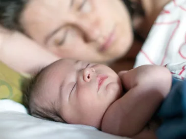 Mother and baby sleeping peacefully together in bed, baby in the foreground.