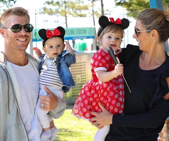 A smiling family with two children dressed in Minnie Mouse outfits outdoors.