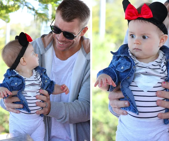 Man holding baby in striped outfit and Minnie Mouse headband, both smiling and looking at each other brightly.
