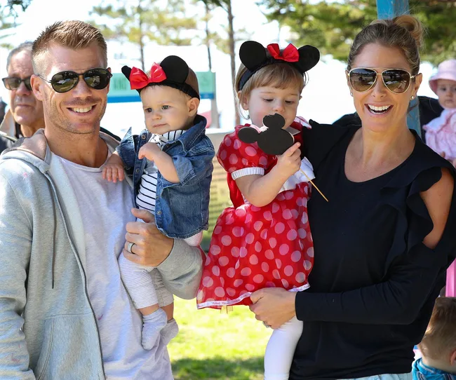 A family with two kids dressed as Minnie Mouse smiling outdoors, one parent wearing sunglasses.