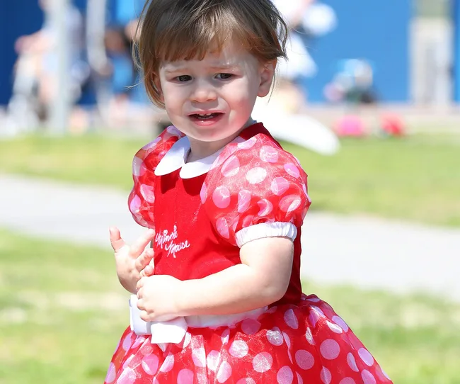 Toddler in a red polka dot dress outdoors, looking slightly upset.