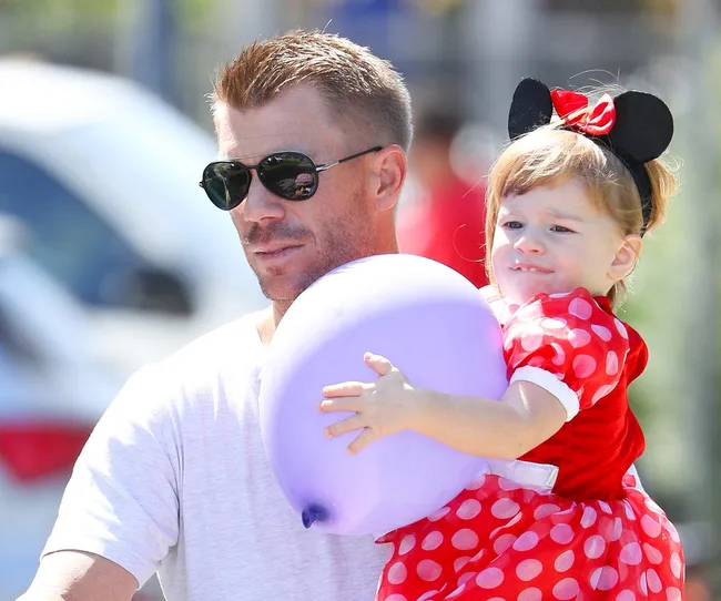 Man carrying a child in a Minnie Mouse outfit holding a purple balloon.