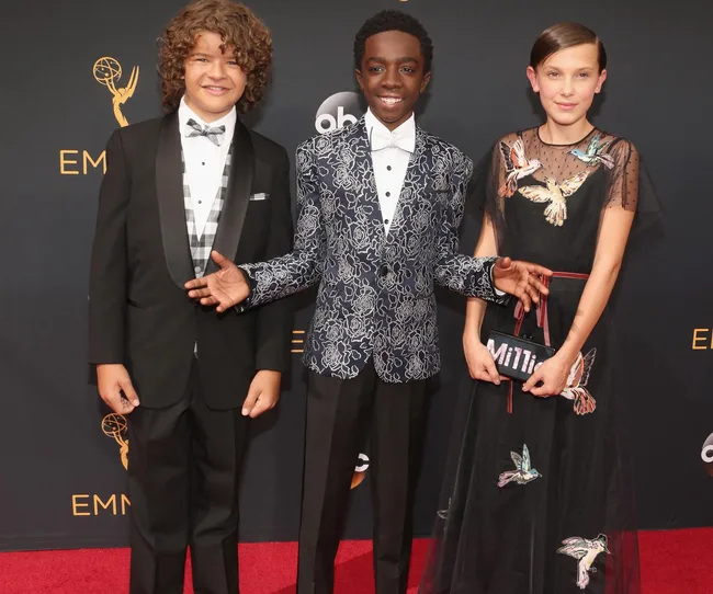 Three young actors on the red carpet at an award event, smiling and dressed in formal attire.