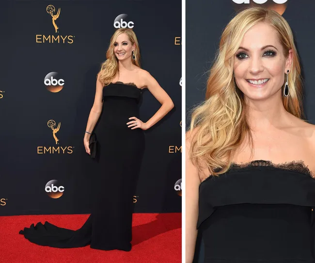A woman in a black strapless gown poses on the red carpet at the Emmys, smiling with long, wavy blonde hair.