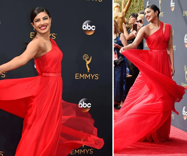 Red carpet event with a smiling woman in a flowing red gown, posing gracefully in front of the Emmy Awards backdrop.