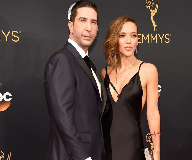 Two individuals posing on the red carpet at an event, wearing formal attire with an Emmy award backdrop.
