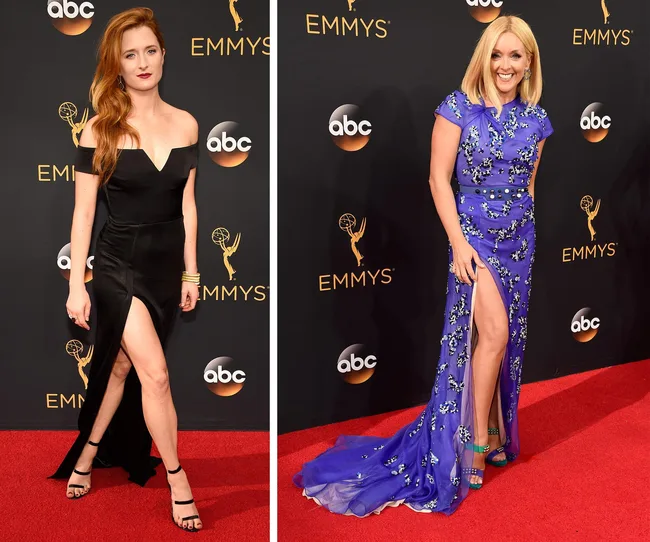 Two women on the Emmy Awards red carpet wearing elegant dresses with thigh-high slits; one in black, the other in blue.
