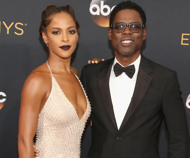 A man in a tuxedo and glasses stands with a woman in a beaded dress on a red carpet with the ABC logo in the background.