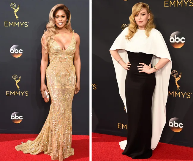 Two women posing on the Emmys red carpet, one in a gold gown, the other in a black and white dress with a cape.
