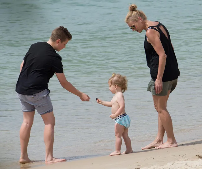 A woman, a teenager, and a toddler playing by the sea on a sandy beach.