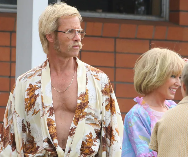 Man with glasses and mustache in patterned robe beside smiling woman in colorful outfit.