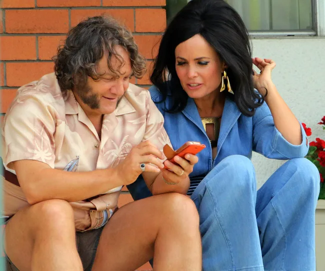 Two people dressed in vintage style looking at a smartphone together on a porch.