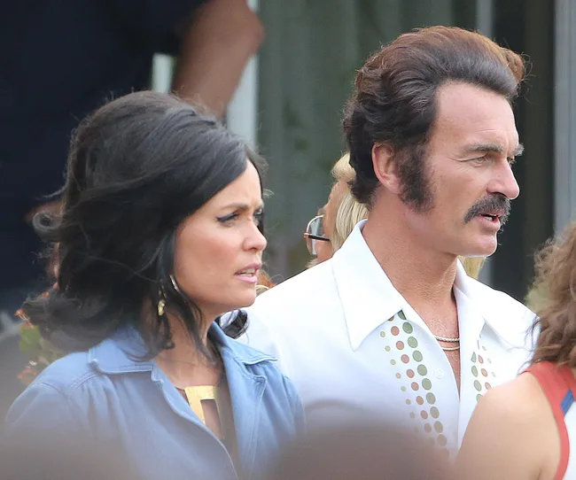Pair dressed in vintage attire, woman in blue with dark hair and man with mustache in white shirt with polka dot accents.