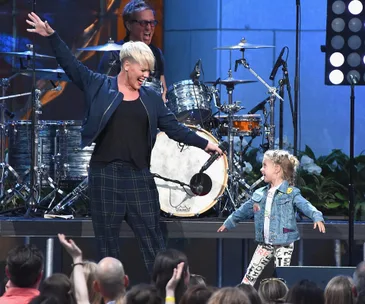 Singer energetically performs on stage with a delighted young girl, both smiling at each other amidst audience applause.
