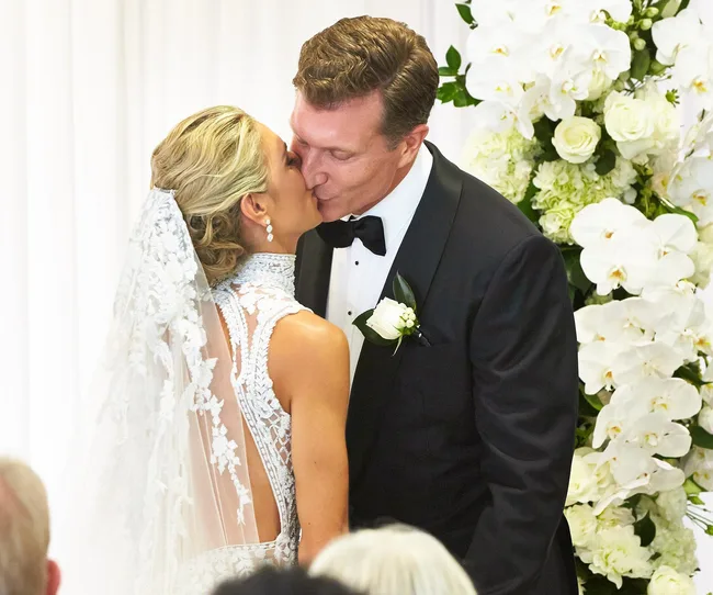 A bride and groom kissing at their wedding, surrounded by white flowers.