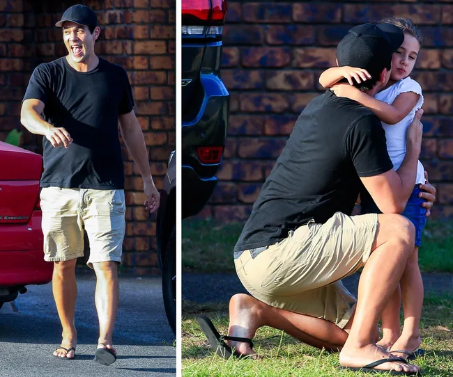 Man in black cap and t-shirt, beige shorts, joyful, hugs a child in white t-shirt outdoors.