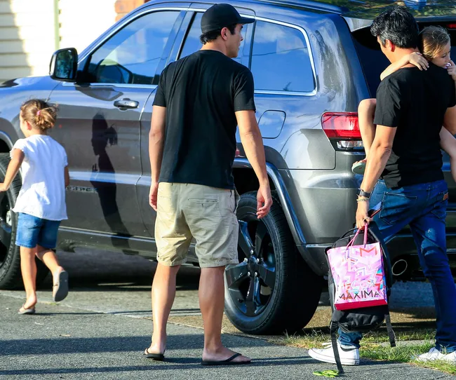 Family near an SUV; a man carries a child while another walks alongside, and a girl runs ahead on the street.