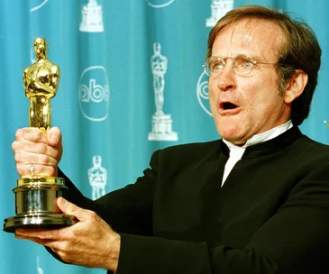 Robin Williams holds an Oscar award with an excited expression at an award ceremony.