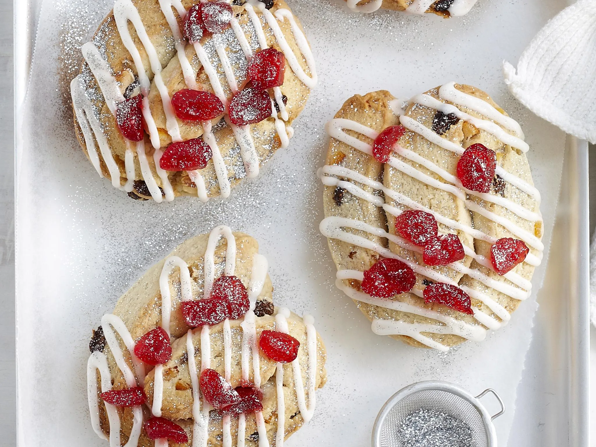 Assorted cookies with white icing, red cherries, and powdered sugar on a tray for festive holiday treats.