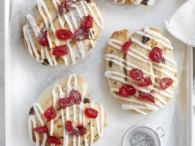 Assorted cookies with white icing, red cherries, and powdered sugar on a tray for festive holiday treats.