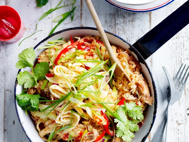 Pan of fried rice with sliced omelette, green onions, red peppers, and cilantro, on a wooden table with a wooden spoon.