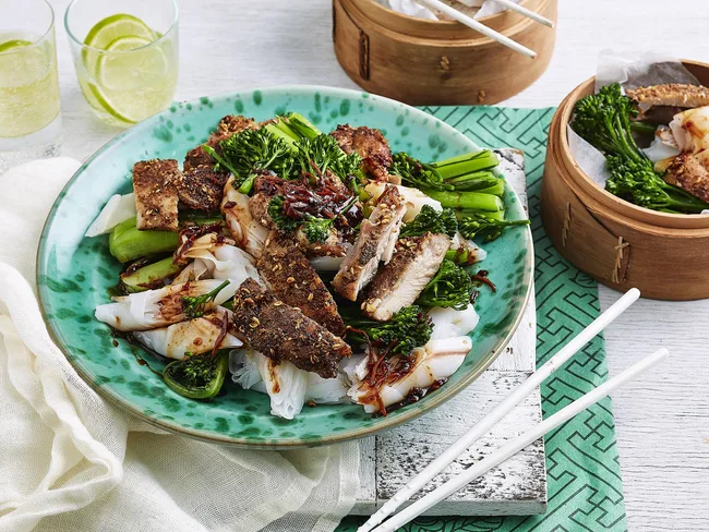 Dish of roasted chicken, broccoli, and noodles on a green plate with chopsticks and glasses of lime drink nearby.