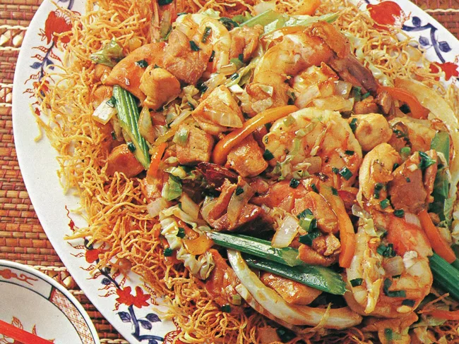 Stir-fried shrimp and vegetables on crispy noodles, served on a decorative plate with floral patterns.