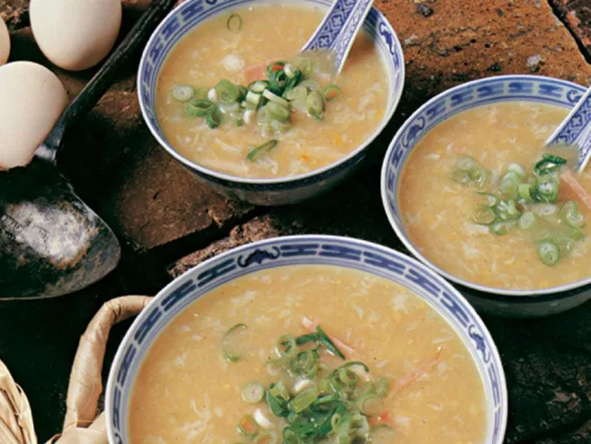 Three bowls of egg drop soup garnished with green onions, set on a rustic surface with eggs nearby.