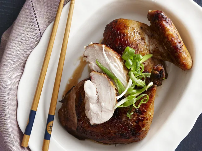 Grilled chicken garnished with green onions on a white plate, accompanied by wooden chopsticks.