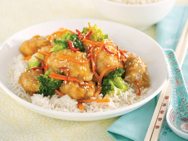 Chicken and broccoli with carrots on rice, garnished with sesame seeds, served with chopsticks.