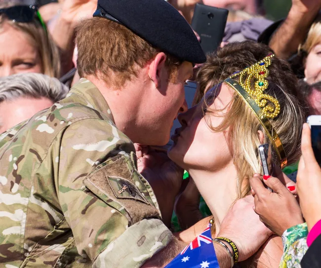 A man in a military uniform kisses a woman wearing a crown in a crowd.
