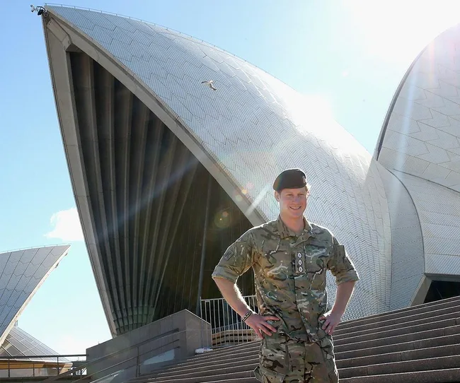 Military-clad person stands in front of the Sydney Opera House under a clear blue sky.