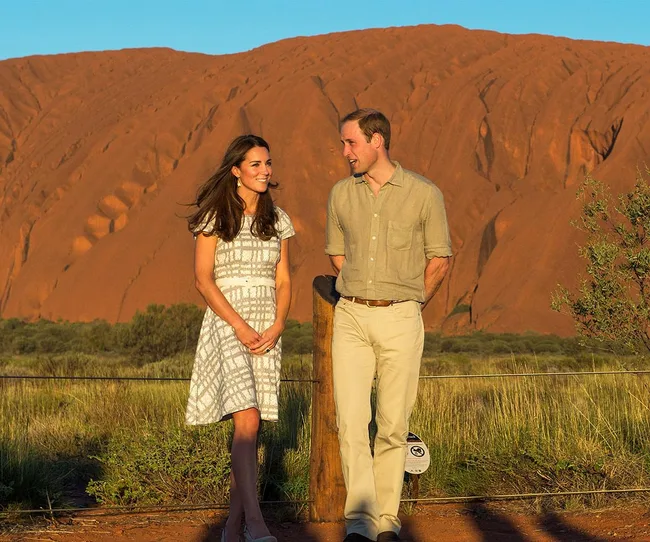 A couple stands smiling in front of a large red sandstone formation under a clear blue sky.