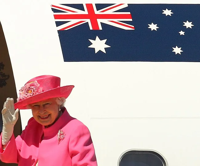 A woman in a pink outfit waves, standing near an aircraft with the Australian flag on it.