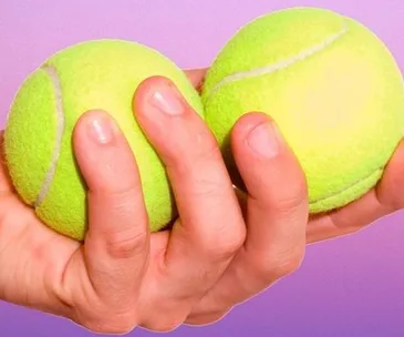 Hand holding two yellow tennis balls against a purple background.