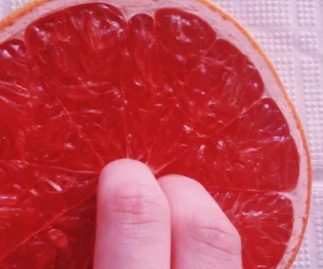 Fingers touching a half-cut grapefruit on a textured surface.