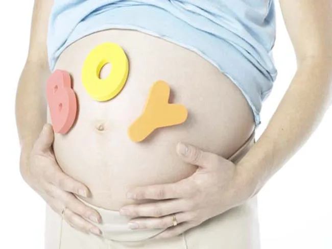 Pregnant belly with "BOY" in colorful letters, hands gently holding the stomach.