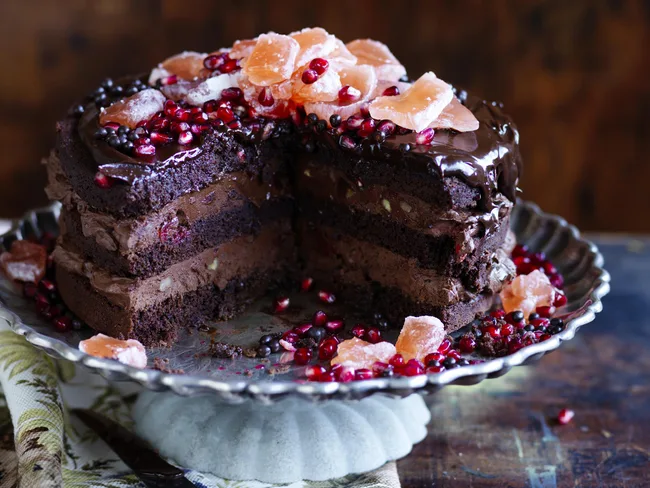Chocolate Christmas cake with ganache, topped with pomegranate seeds and candied fruits on a rustic metal platter.