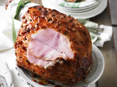 Fig-glazed ham with cloves on a serving platter, partially sliced.