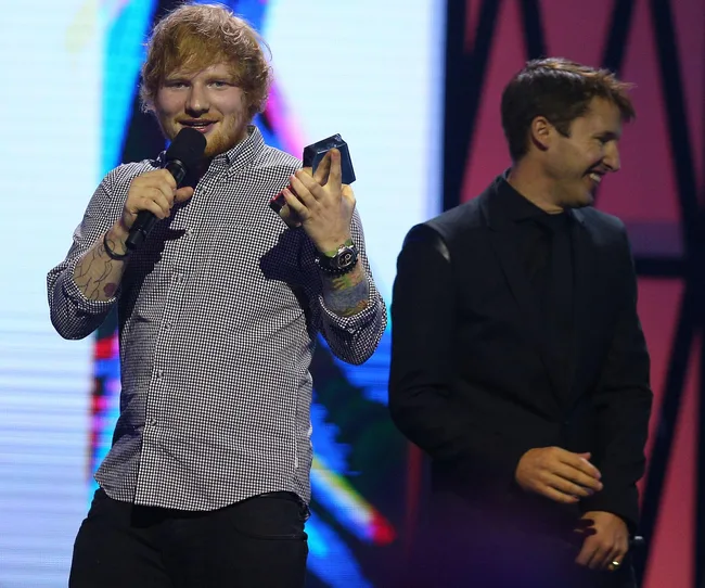 "Two men on stage, one holding an award and microphone, smiling at an event."