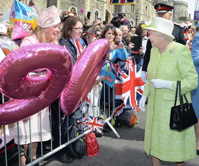 "Queen Elizabeth II in lime green coat greets crowd holding pink '90' balloons and Union Jack flags during celebration."