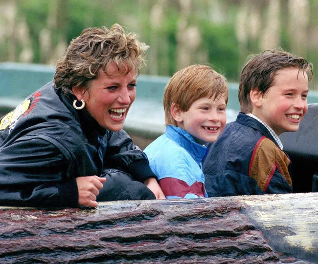 A woman and two young boys laughing together on a log ride at an amusement park.