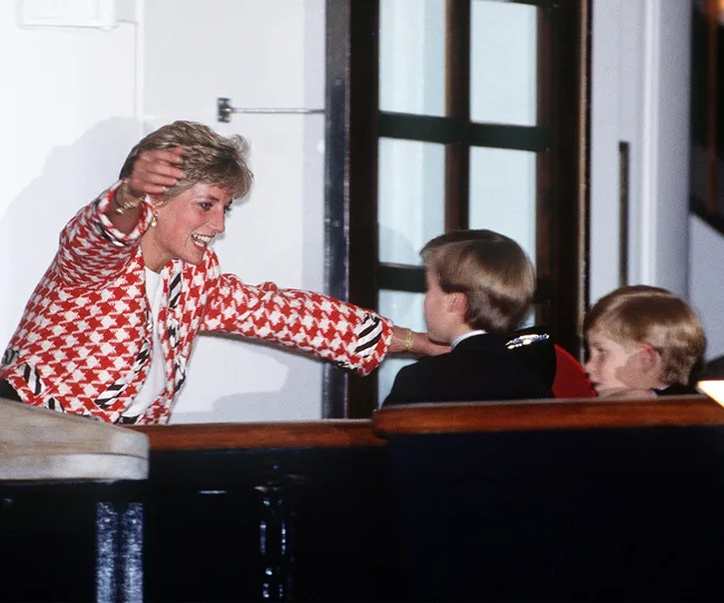 Diana hugs her two sons warmly, wearing a red patterned jacket in a candid, joyful moment.