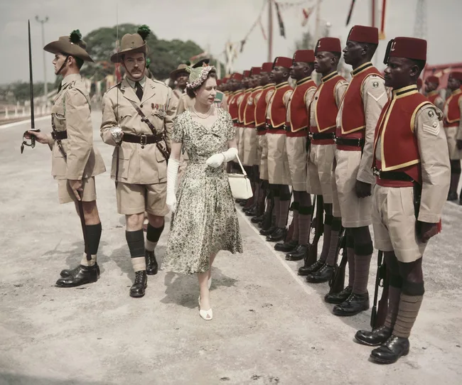 A woman in a floral dress walks past a row of uniformed soldiers standing at attention during a ceremonial event.
