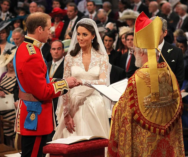 A royal couple exchanging vows during their wedding ceremony in front of a priest, with guests in the background.