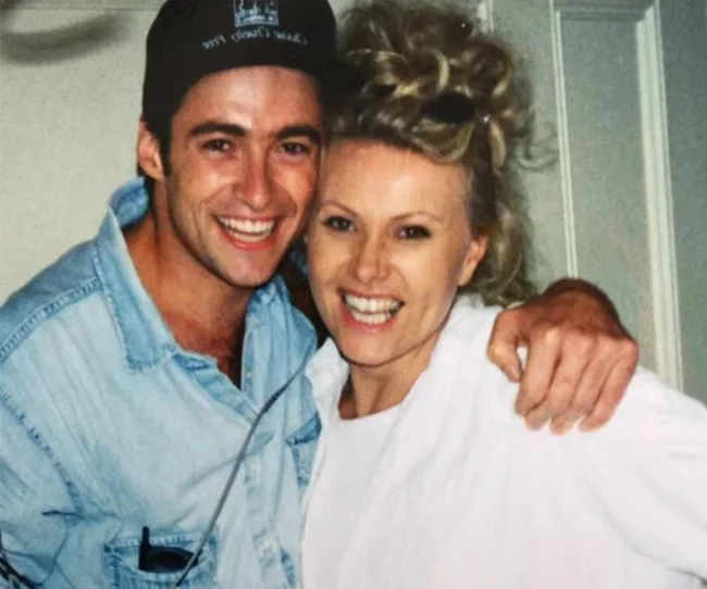 A smiling man in a denim shirt and cap embraces a smiling woman with curly blonde hair in front of a door.