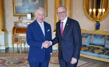 Two men in suits shaking hands in an elegantly decorated room with ornate furnishings and artwork.