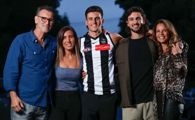 A group of five people, including a person in a black and white sports jersey, smiling outdoors.
