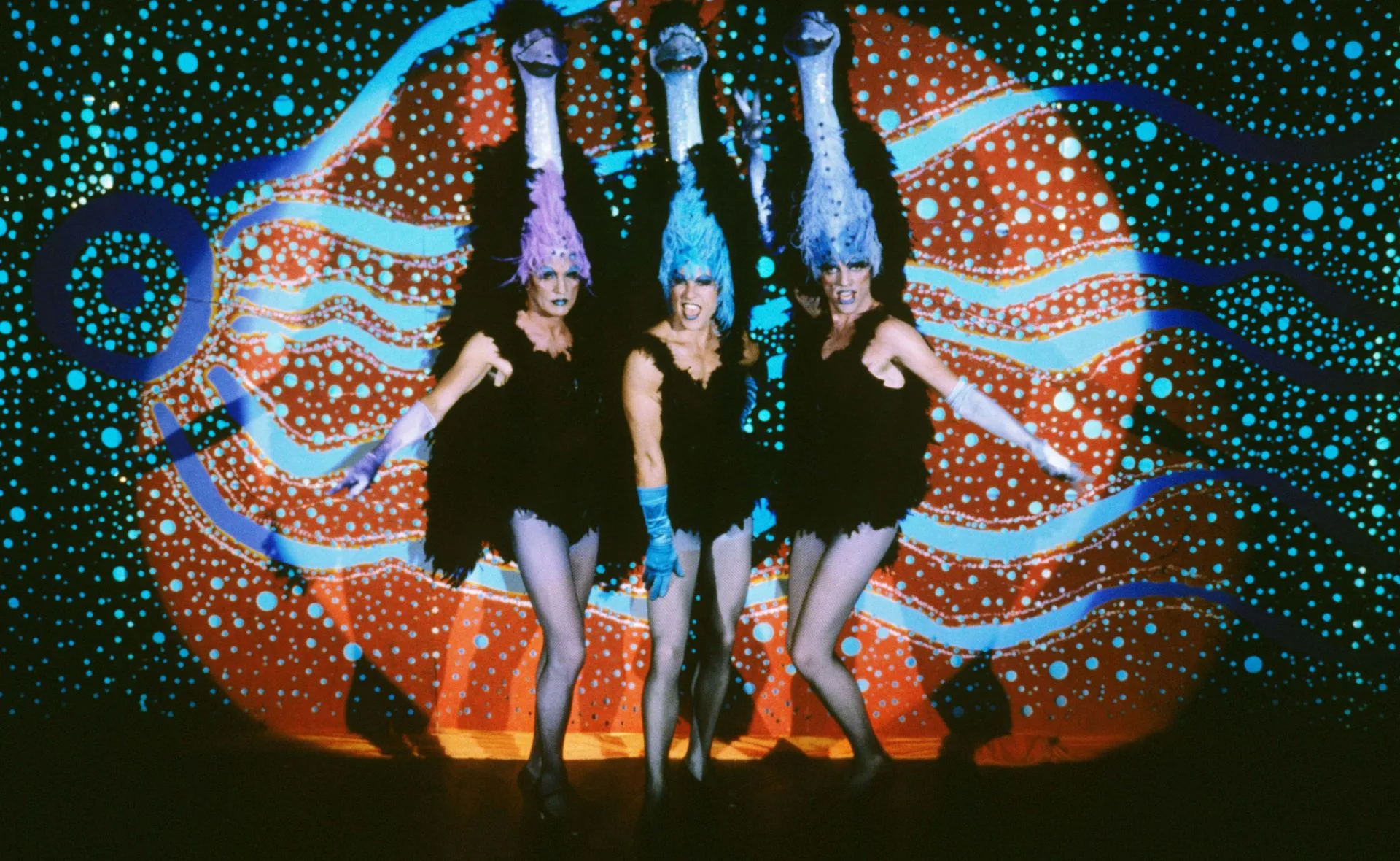 Priscilla takes the stage in blue hair, black mini dress and fishnet stockings along with two others