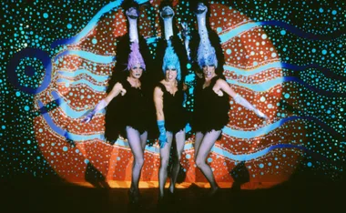Priscilla takes the stage in blue hair, black mini dress and fishnet stockings along with two others